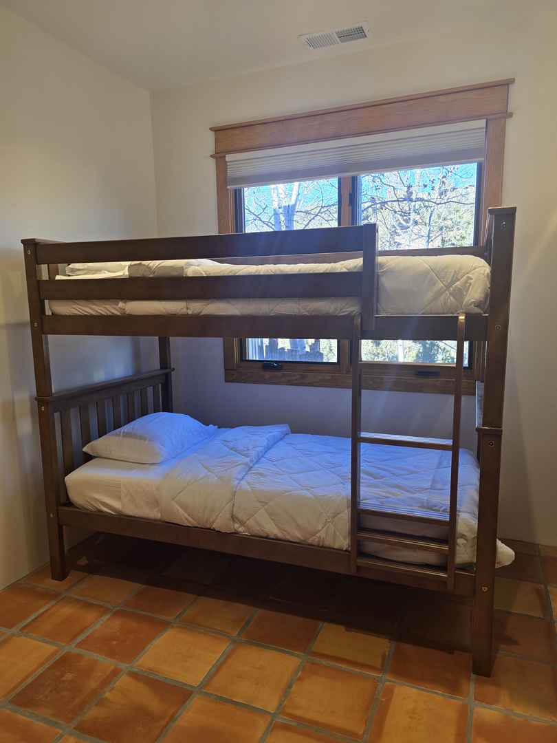 Rest comfortably in your cozy bunk bed setup, where natural light streams through the window and warm earth tones create a peaceful retreat.