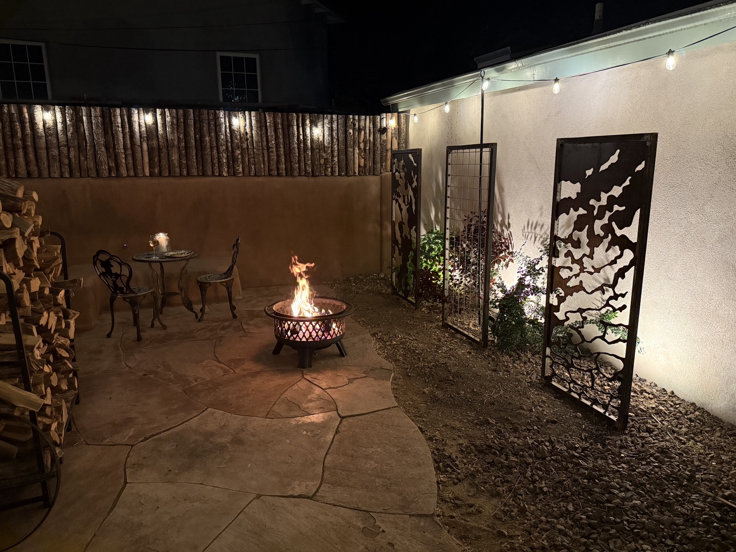 Gather around your private fire pit under the stars—perfect for cozy evenings after a day of exploring. String lights cast a warm glow over artful metal accents and comfortable seating, creating your own peaceful outdoor retreat.