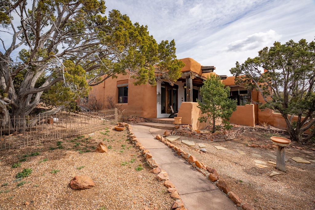 Adobe-style retreat nestled among mature trees with natural desert landscaping and welcoming entrance pathway.
