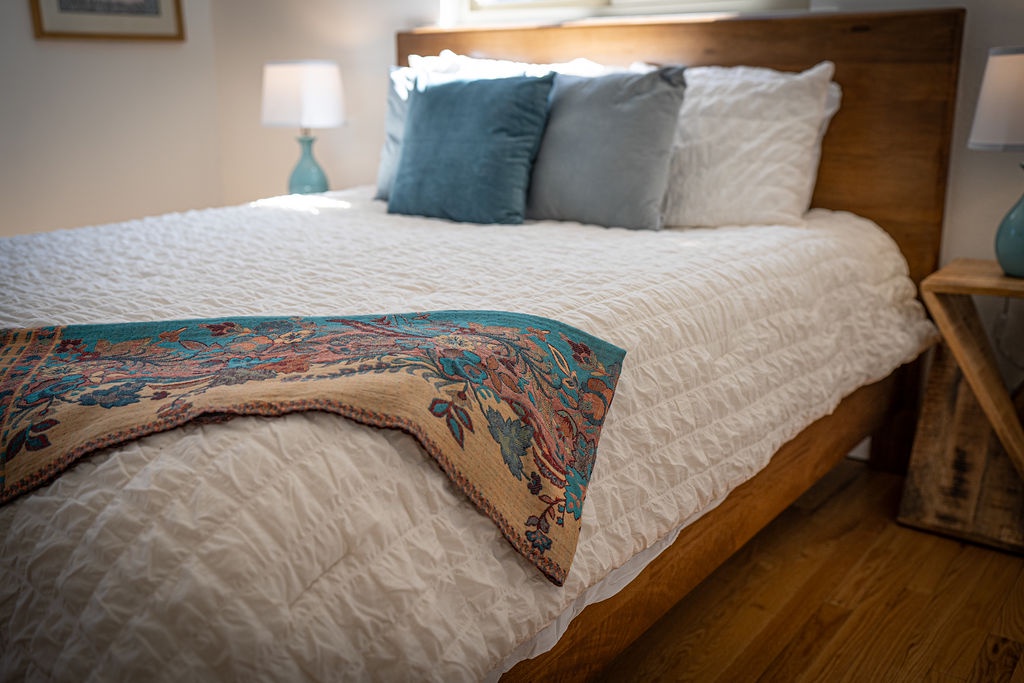 Sink into plush bedding with a colorful throw draped invitingly across crisp white linens and soft teal pillows.