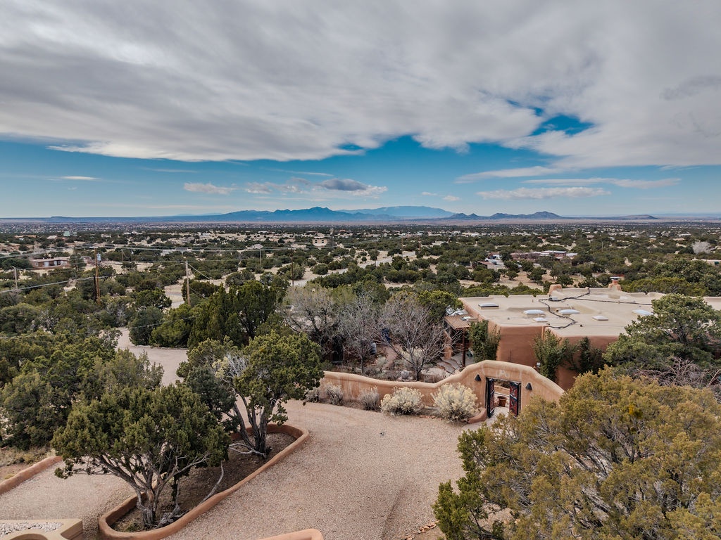 Elevated aerial view of Southwestern adobe-style property nestled among desert vegetation with distant mountain ranges.