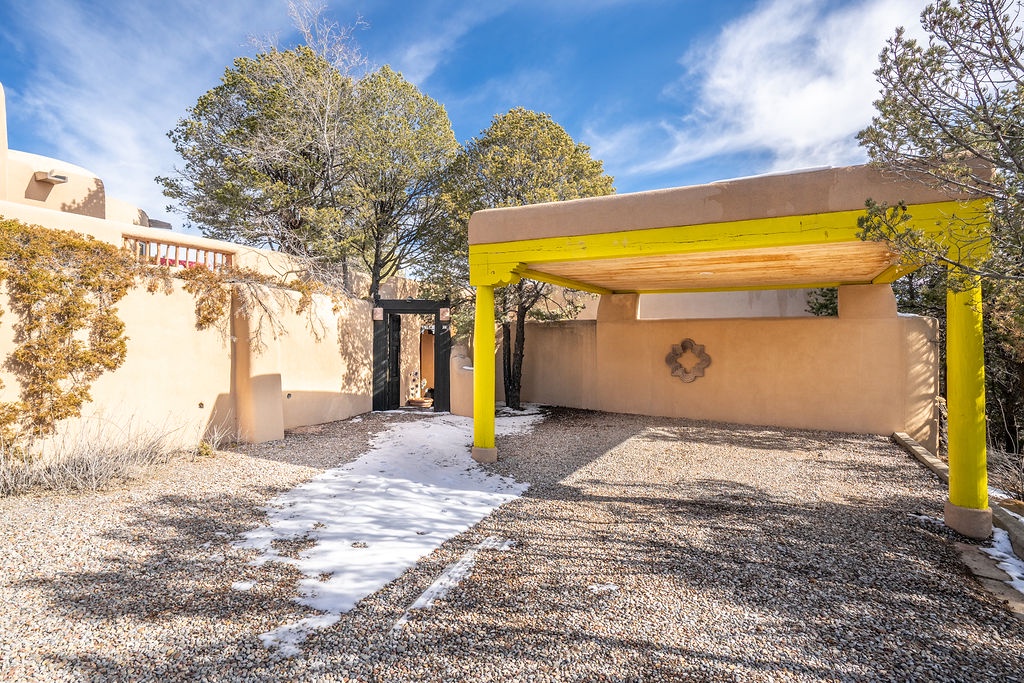 Adobe-style property with covered parking and decorative entrance gate set among mature trees.