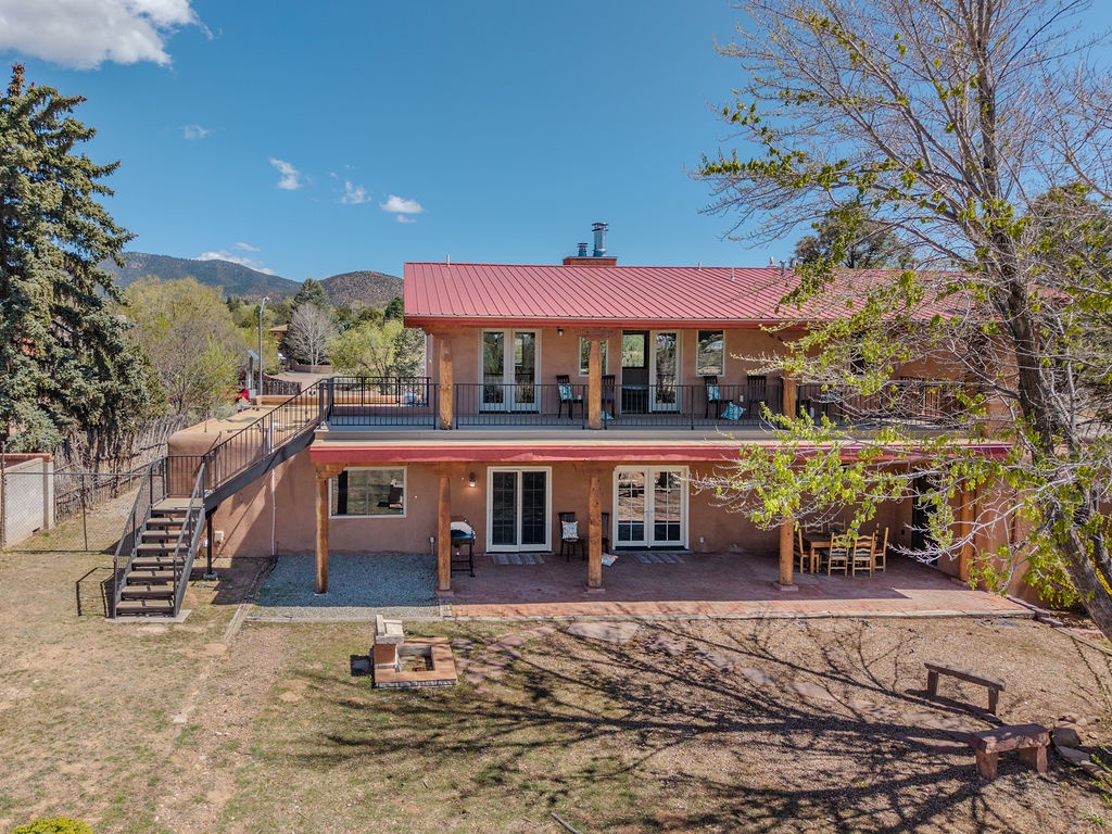 A welcoming two-story mountain retreat with red metal roof nestled among trees, featuring outdoor patios and stunning mountain backdrop.