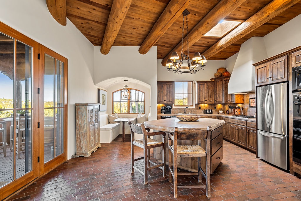 Your rustic kitchen features exposed wooden beams, a large island, and French doors opening to outdoor dining spaces.
