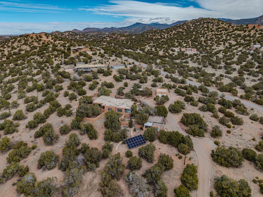 Aerial view of a secluded desert property nestled among rolling hills and scattered juniper trees, with solar panels and mountain vistas.