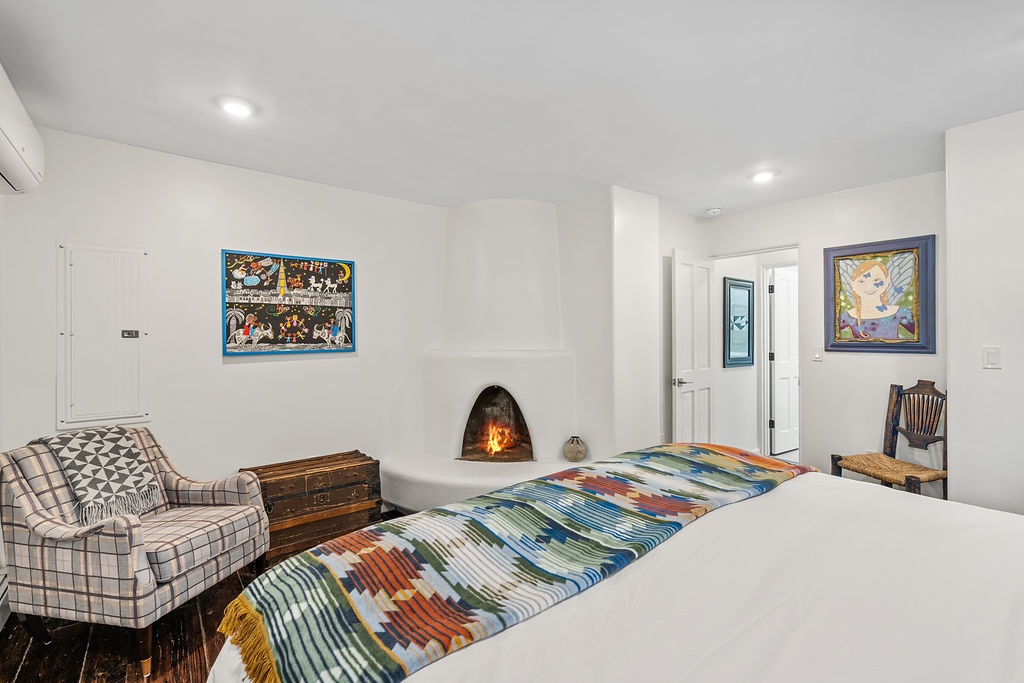 Unwind in your cozy bedroom featuring a crackling kiva fireplace, colorful artwork, and plaid reading chair for ultimate relaxation.