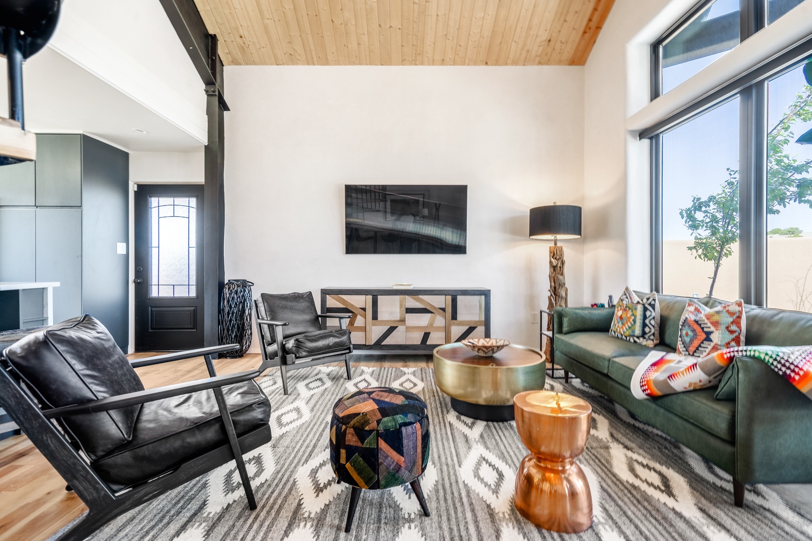 Relax in this stunning modern living room where natural light streams through floor-to-ceiling windows, highlighting the warm wood ceiling and vibrant textiles.