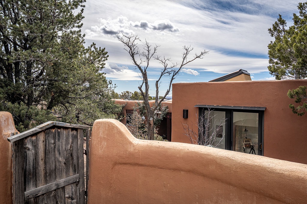 Adobe-style property nestled among mature trees under expansive southwestern skies with distinctive architectural curves and natural landscaping.