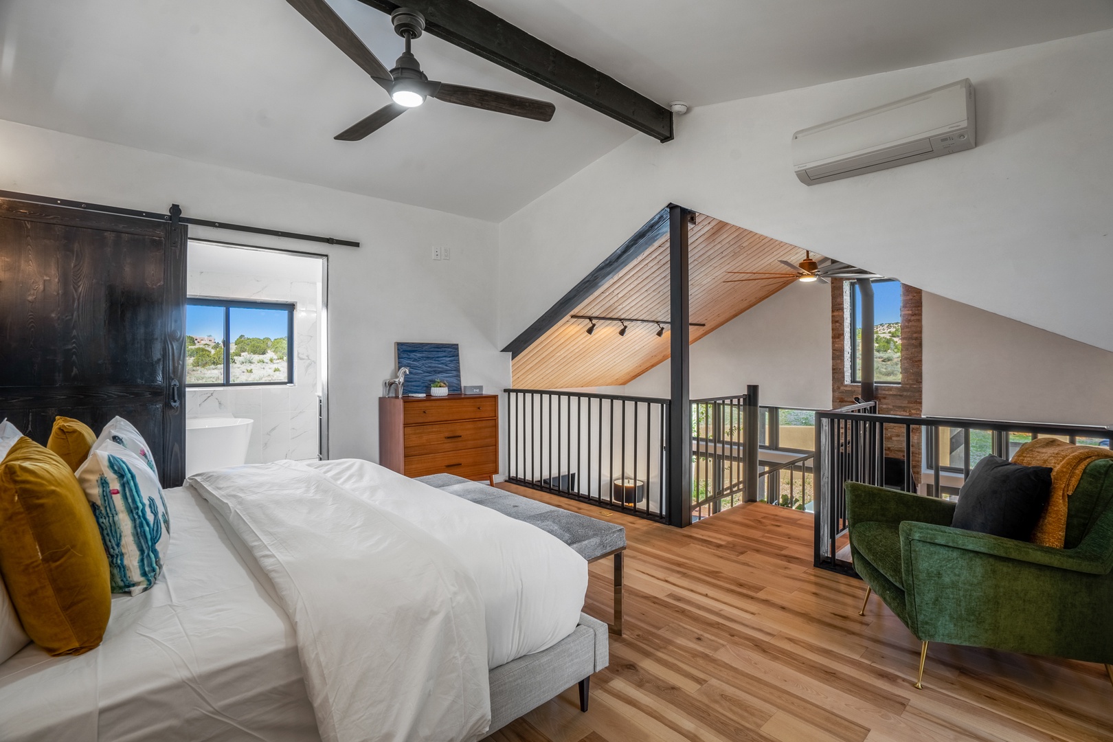 Retreat to your stylish loft bedroom with exposed beams, cozy seating, and peaceful views through large windows.