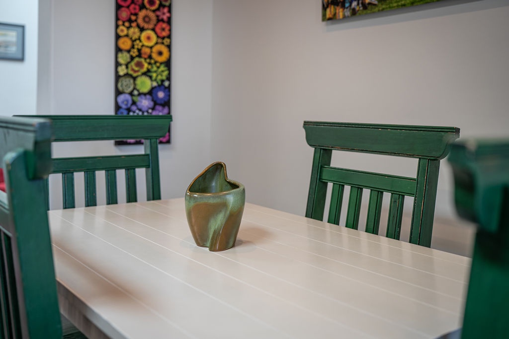 Share meals around this charming wooden table, where green chairs and colorful art create a warm dining atmosphere.
