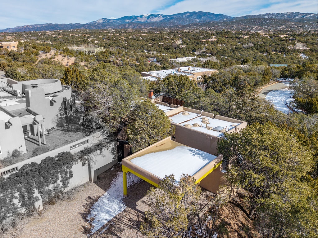 Aerial view of modern adobe-style homes nestled among native trees with snow-dusted mountains creating a stunning backdrop in this high-desert location.
