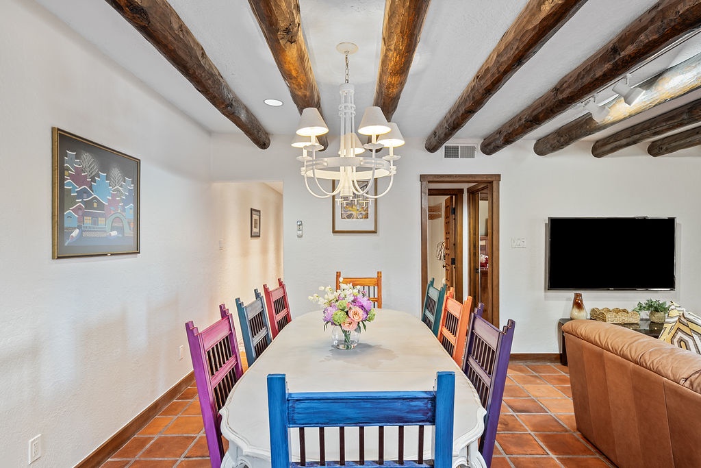 Gather around your rustic dining table with colorful chairs under dramatic wooden beams. The elegant chandelier creates warm ambiance for memorable meals.