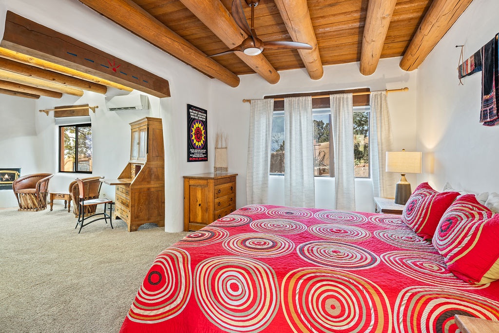Relax in your spacious bedroom featuring rustic wooden beams, vibrant bedding, and bright windows showcasing desert views.