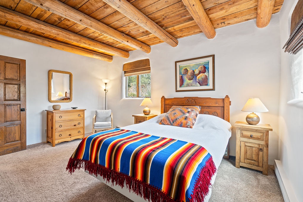 Drift off beneath stunning wooden beams in this cozy bedroom, where vibrant Southwest textiles and warm lighting create your perfect desert retreat.