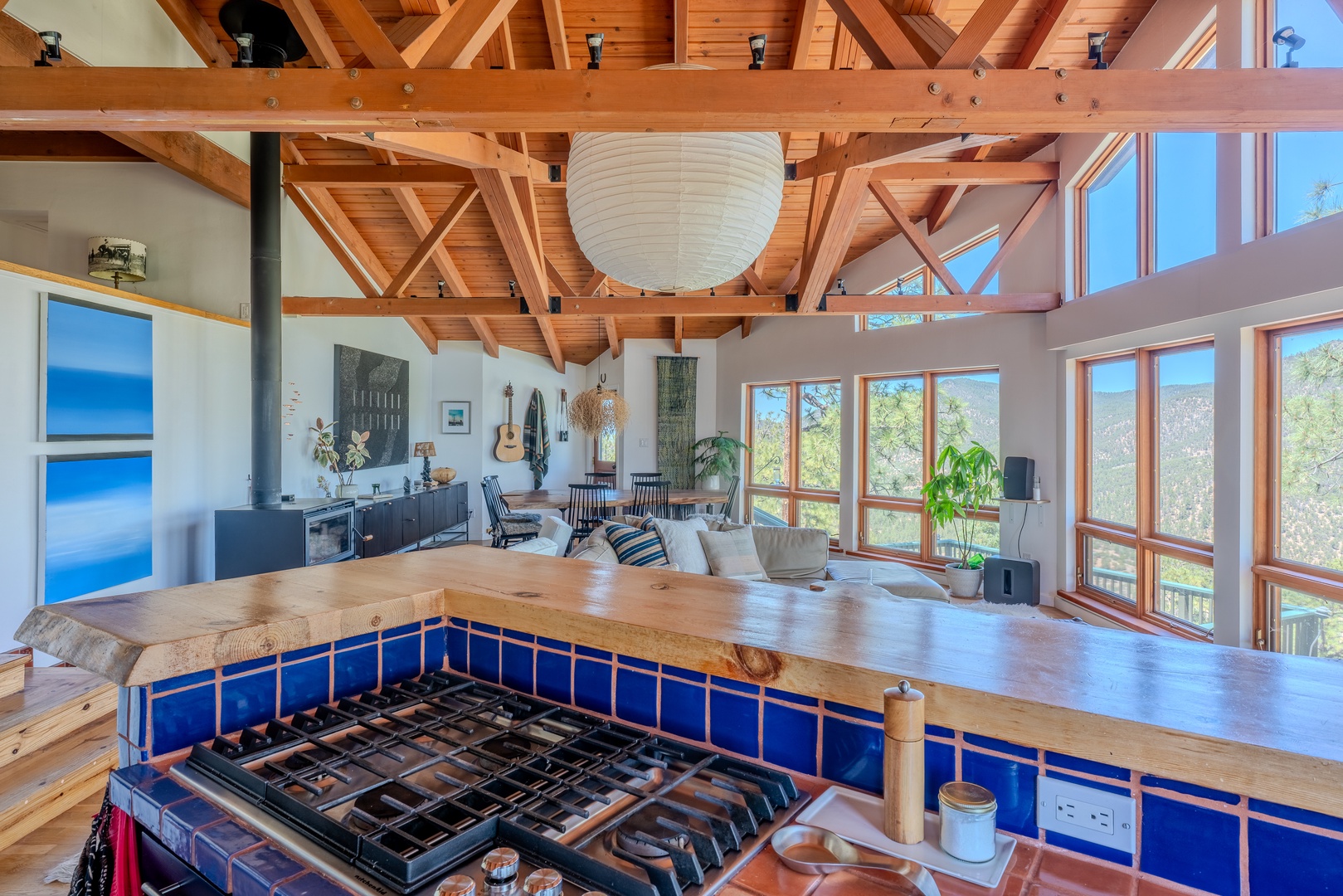 Stunning open-concept living space where exposed timber beams frame your mountain retreat. Cook at the vibrant blue-tiled island while natural light pours through floor-to-ceiling windows, connecting you with nature's beauty.