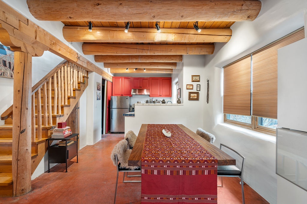 Gather around your rustic dining table beneath stunning exposed beams, where warm wood meets vibrant textiles in this inviting space.
