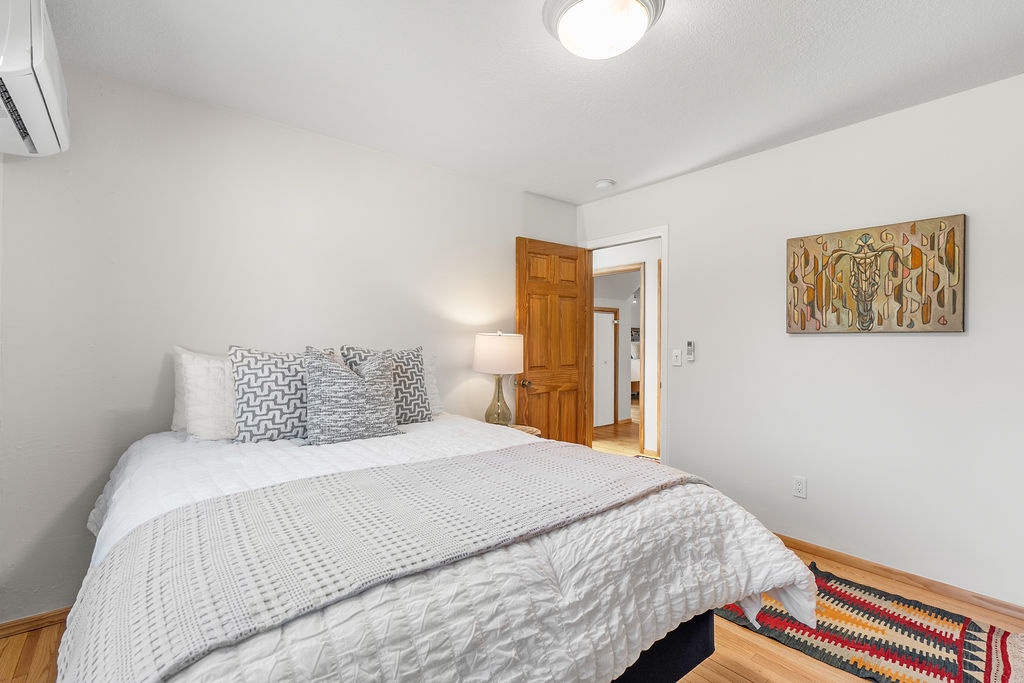 Sink into crisp white linens and textured throws in this serene bedroom, where warm wood floors and thoughtful artwork create your peaceful retreat.