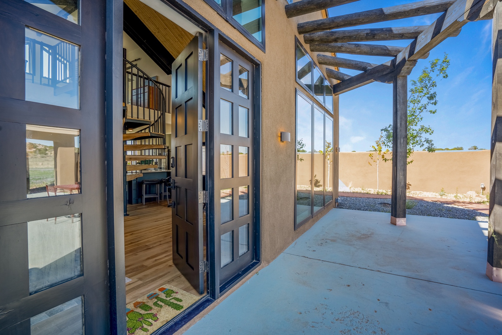 Step into your private covered patio where rustic beams frame desert views and glass doors open to a modern interior with spiral stairs.