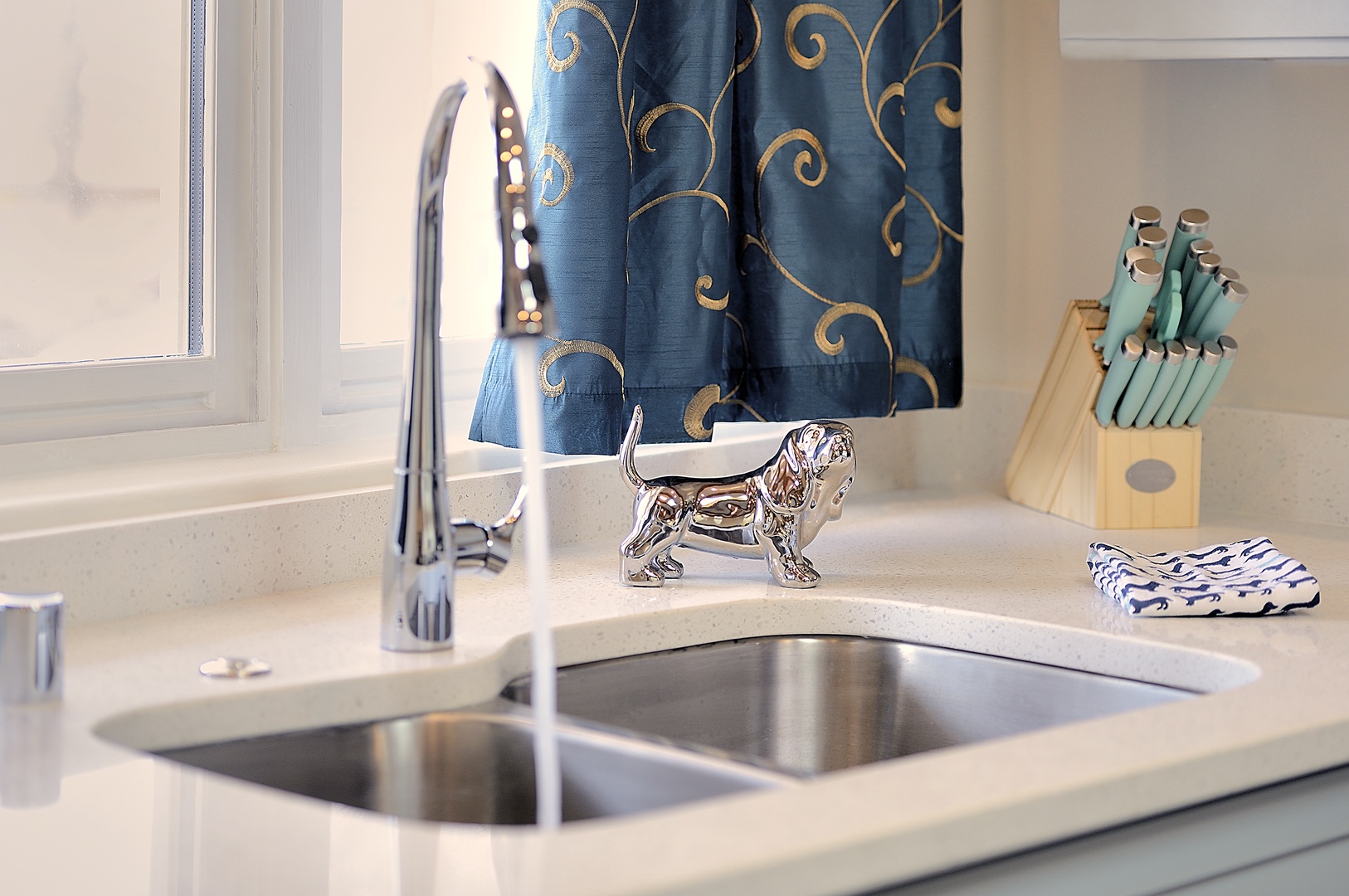 Your kitchen sink area features elegant blue curtains and thoughtful touches like a charming decorative dog figurine that adds personality to your cooking space.