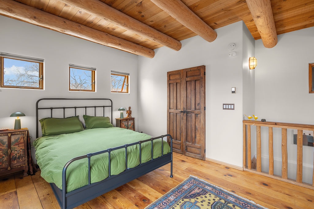 Rest peacefully in your rustic bedroom with exposed wood beams, cozy green bedding, and charming windows framing natural views.