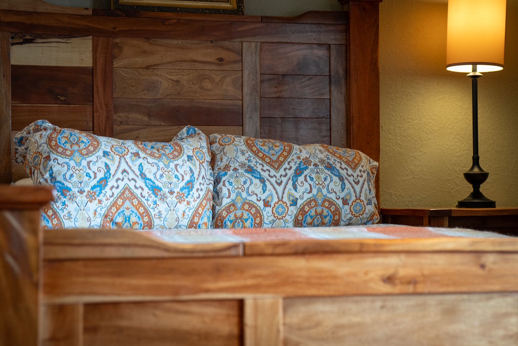 Sink into plush pillows and rustic wood charm in your cozy bedroom retreat, where warm lamplight creates the perfect ambiance for relaxation.
