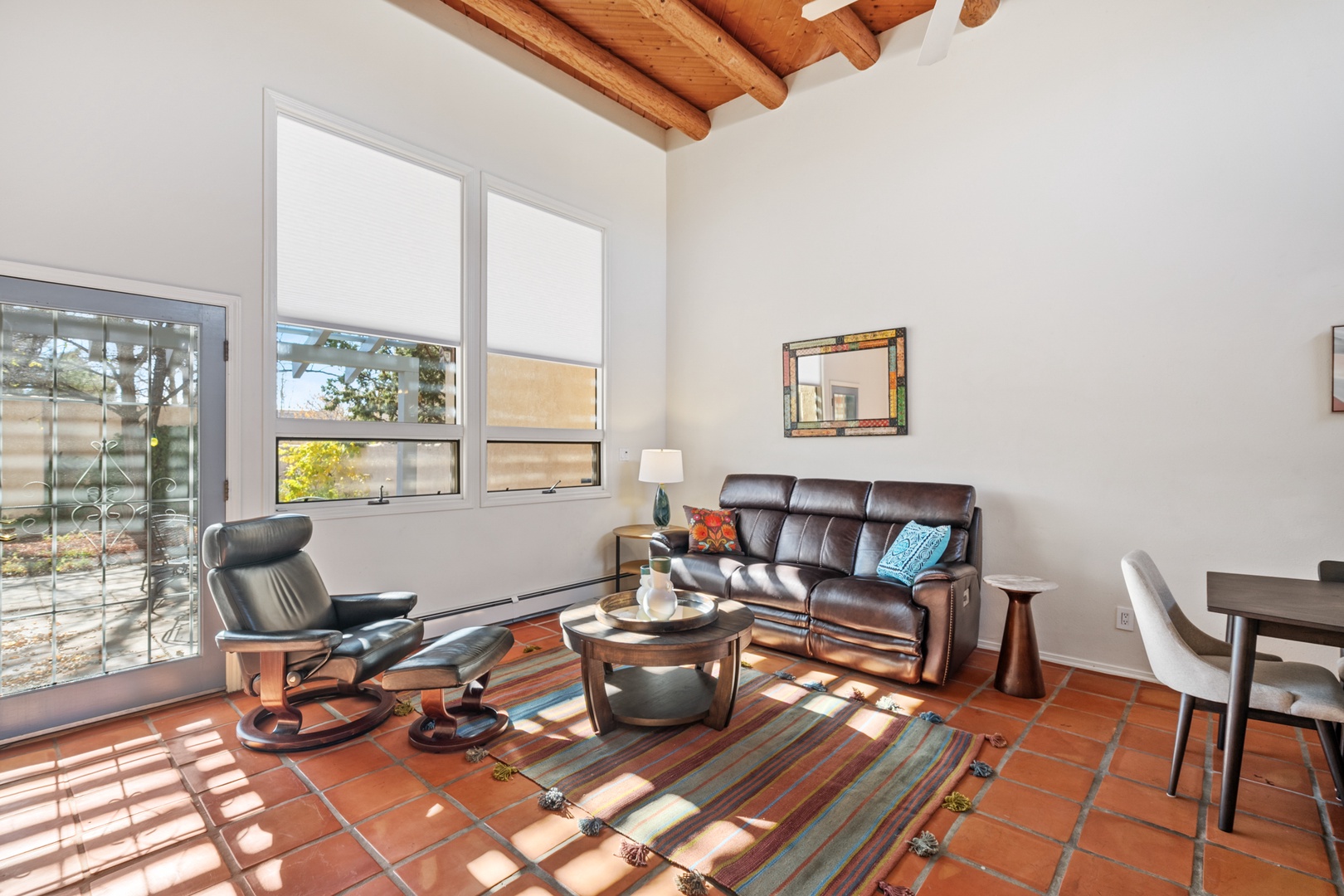 Relax in your stylish living room with exposed wooden beams, comfortable leather seating, and natural light streaming through large windows.