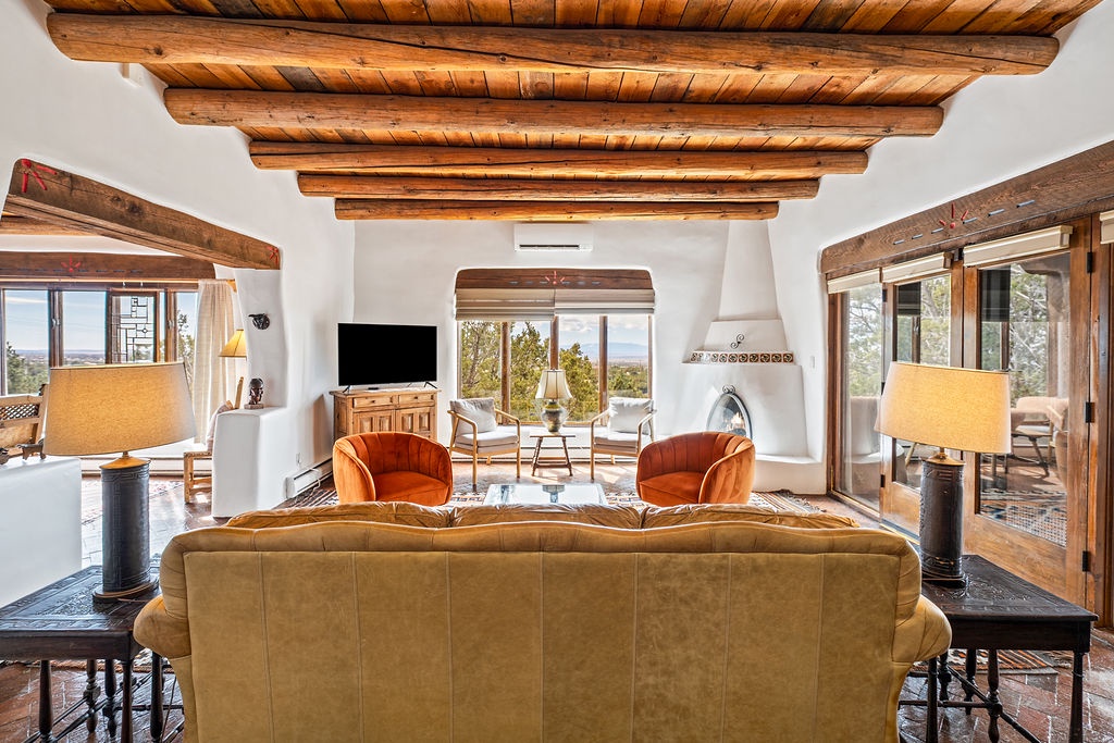 Relax in your stunning southwestern living room featuring exposed wood beams, cozy fireplace, and panoramic views through picture windows.
