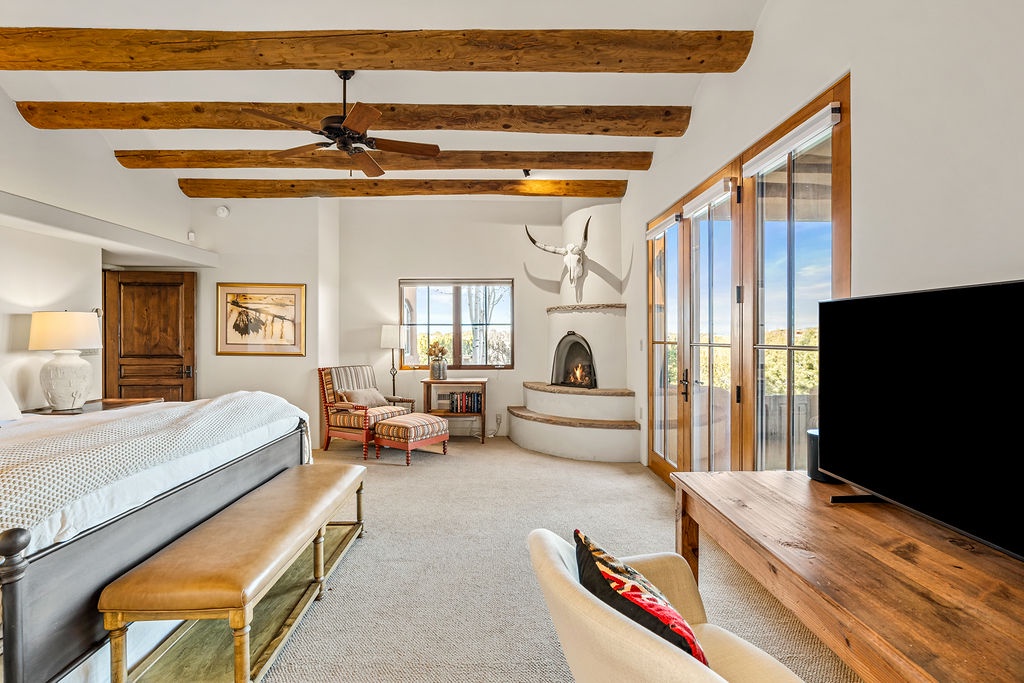 Unwind in your luxurious bedroom featuring exposed wooden beams, a cozy fireplace, and sliding doors opening to beautiful outdoor views.