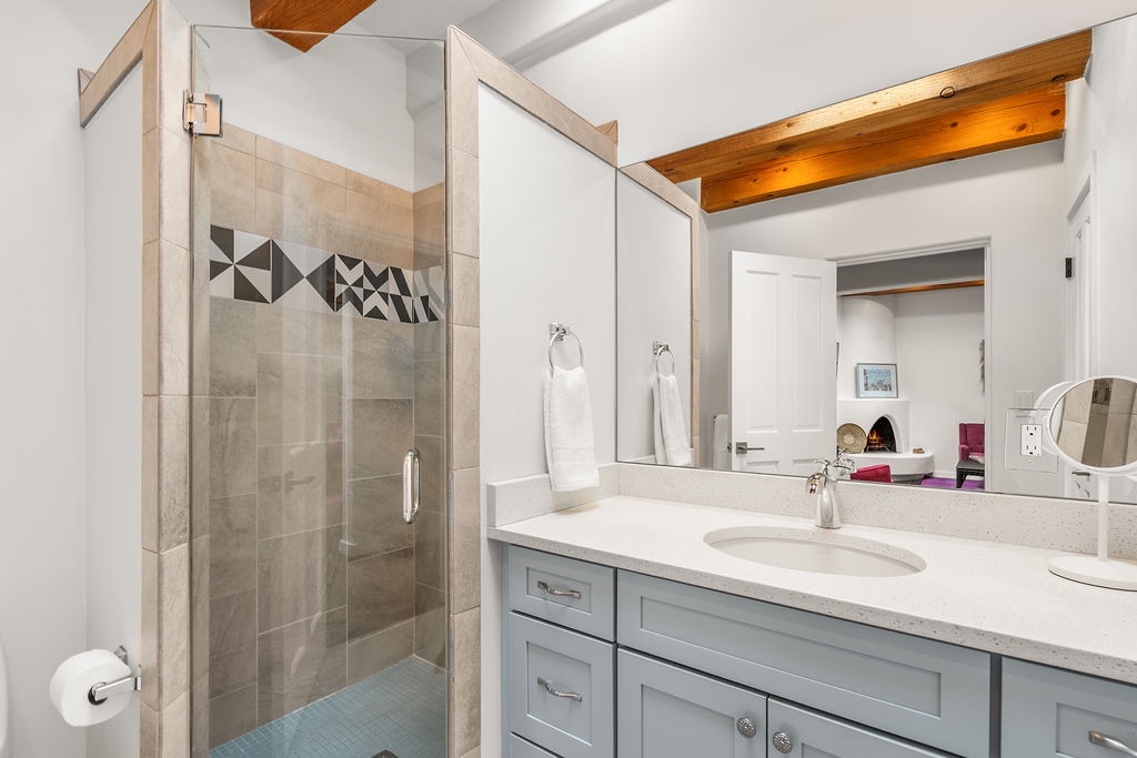 Step into your spa-like sanctuary with a stunning glass-enclosed shower and modern vanity under warm wood beams.