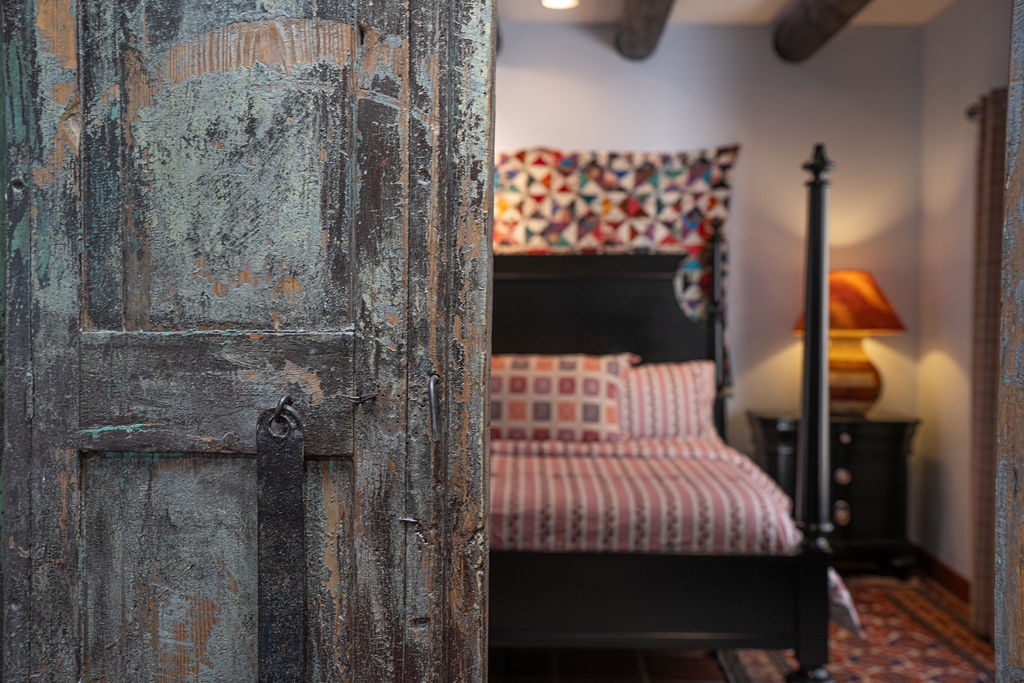 Step into your charming bedroom where rustic wooden doors open to reveal a cozy four-poster bed with vibrant quilted bedding awaiting your restful nights.