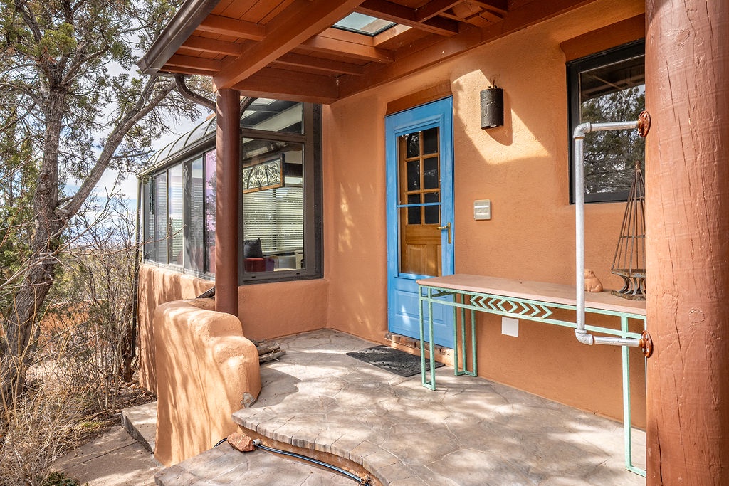 Adobe-style property entrance featuring blue accents and covered porch area surrounded by natural desert landscape.