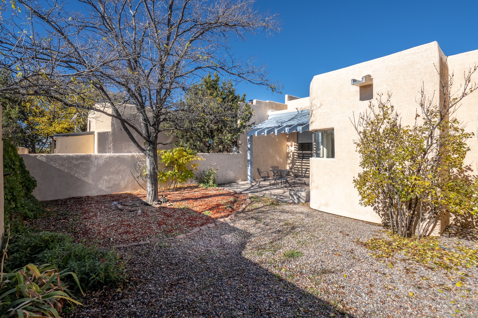 Modern Southwestern-style property featuring clean adobe architecture and native desert landscaping with mature trees and gravel pathways.