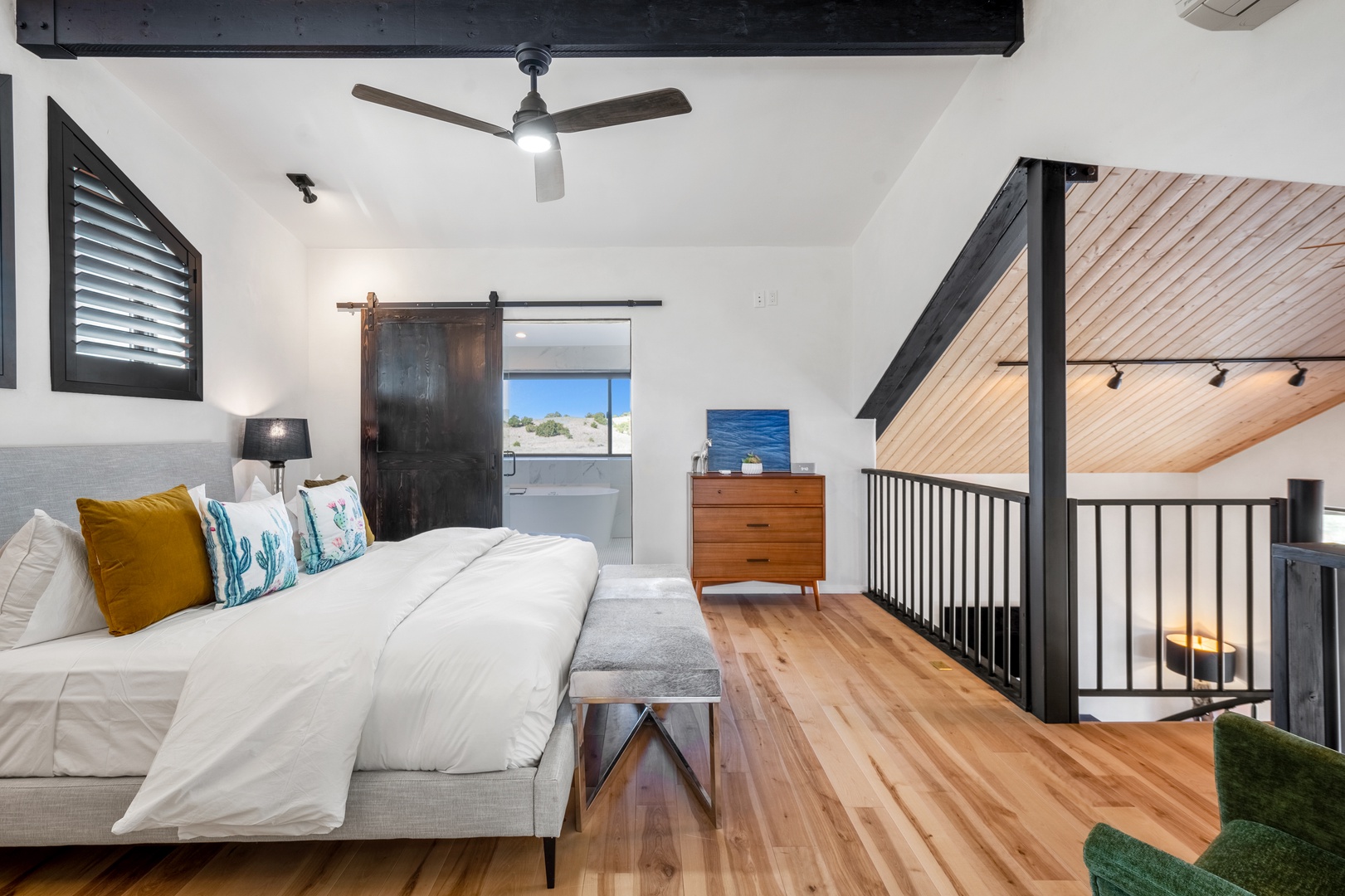 Drift off in this modern loft bedroom where exposed beams meet coastal charm, complete with glimpses of blue waters through your private sliding door.