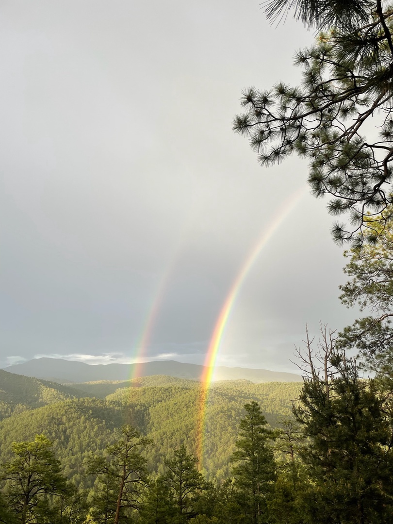 A double rainbow arcs over forested mountain ridges, framing the scenic natural landscape surrounding the property.