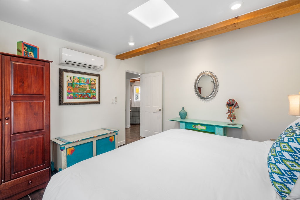 Rest in your serene bedroom featuring vibrant local art, exposed wooden beams, and modern AC comfort for perfect temperature control.