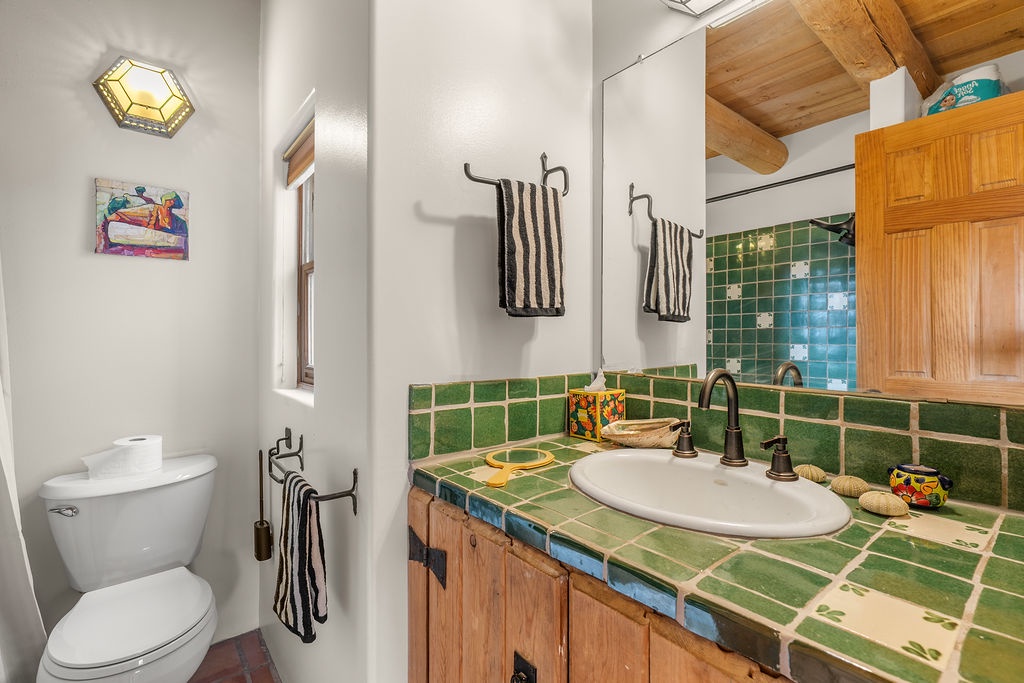 Step into your charming bathroom featuring handcrafted green tiles, rustic wood beams, and authentic Mexican pottery that creates a warm, artistic atmosphere.