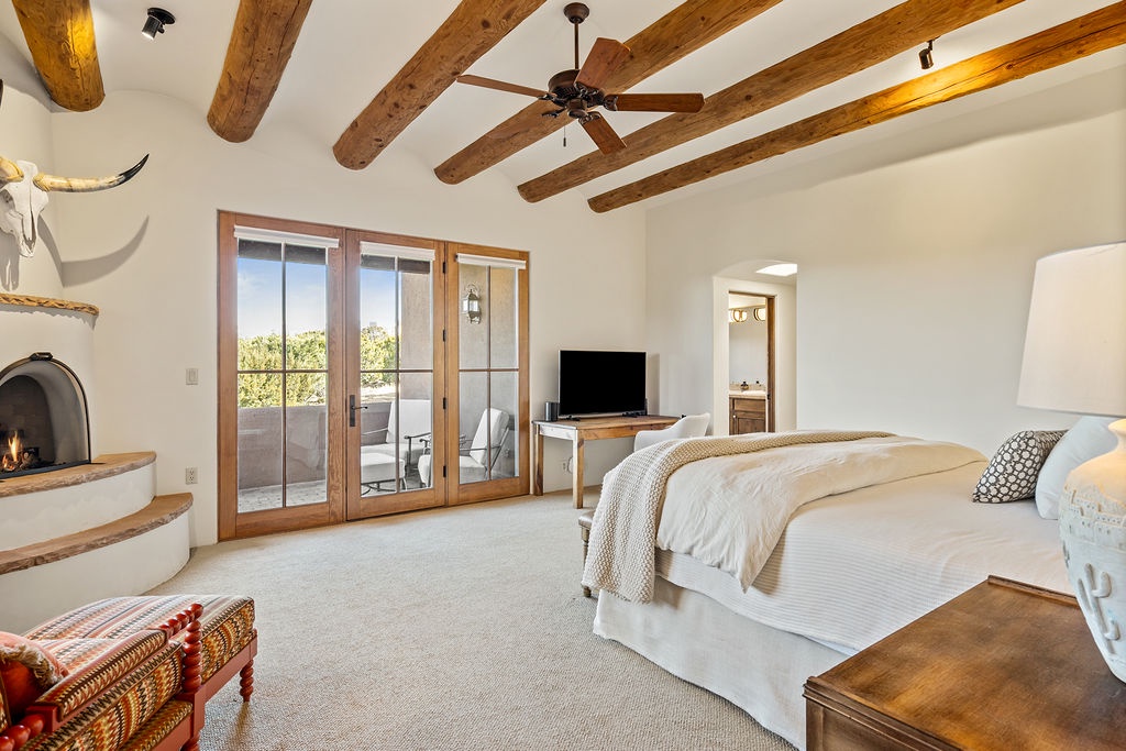 Drift off under rustic beams in this serene bedroom featuring a cozy fireplace and private terrace for peaceful mornings.