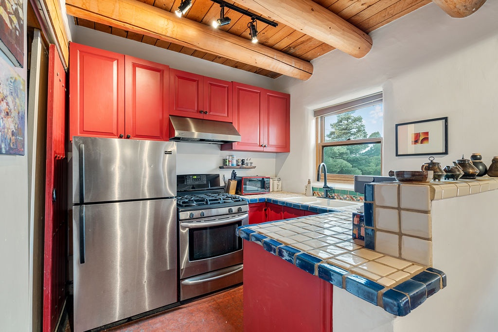 Your vibrant kitchen features bold red cabinets, exposed wood beams, and rustic tile counters—perfect for preparing meals with style.