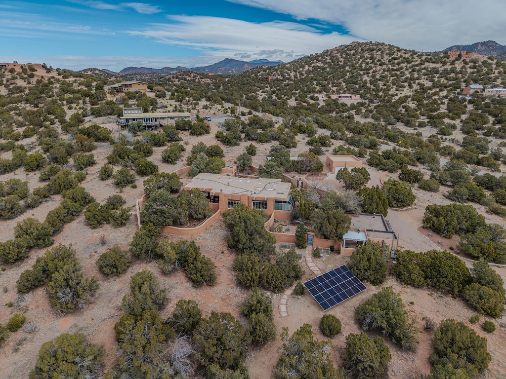 Aerial view of a secluded desert retreat nestled among rolling hills and natural vegetation in a peaceful mountain setting.