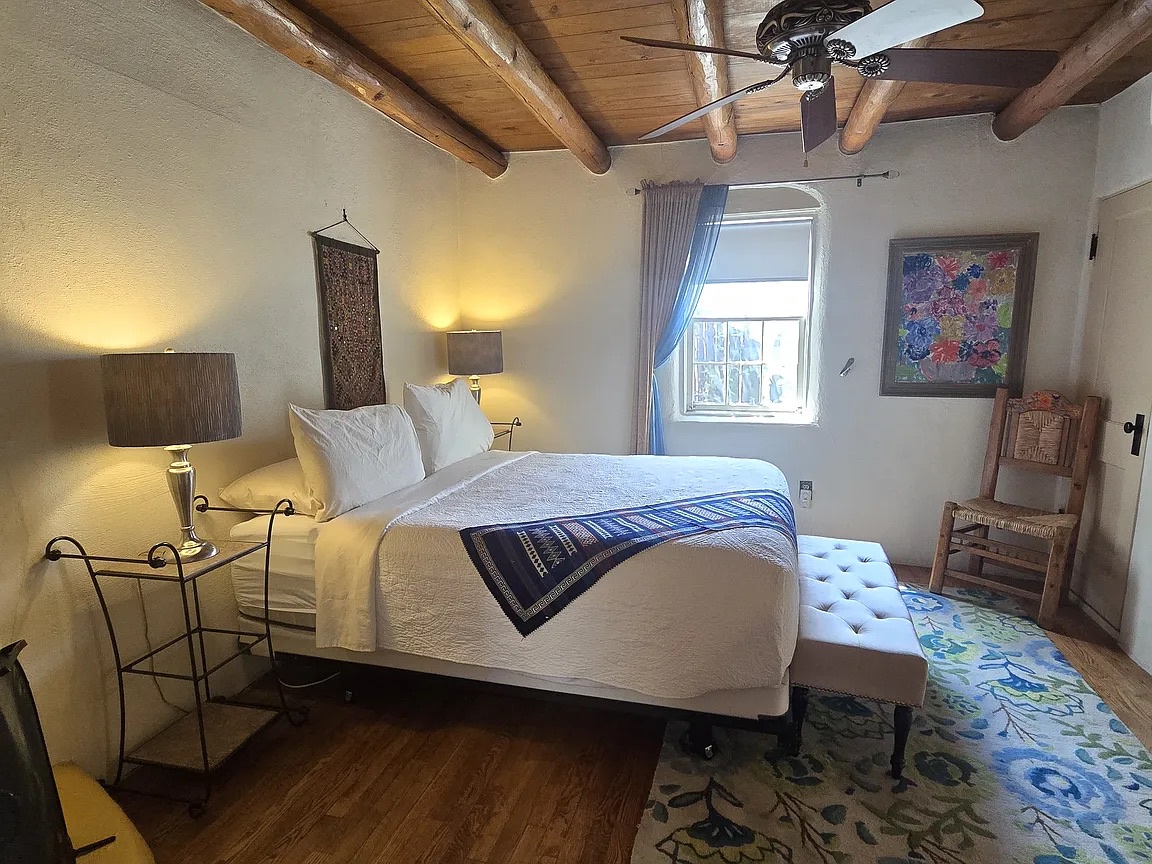 Unwind under rustic timber beams in your cozy bedroom, where warm lighting, a plush bed, and southwestern charm create your perfect retreat after exploring the area.