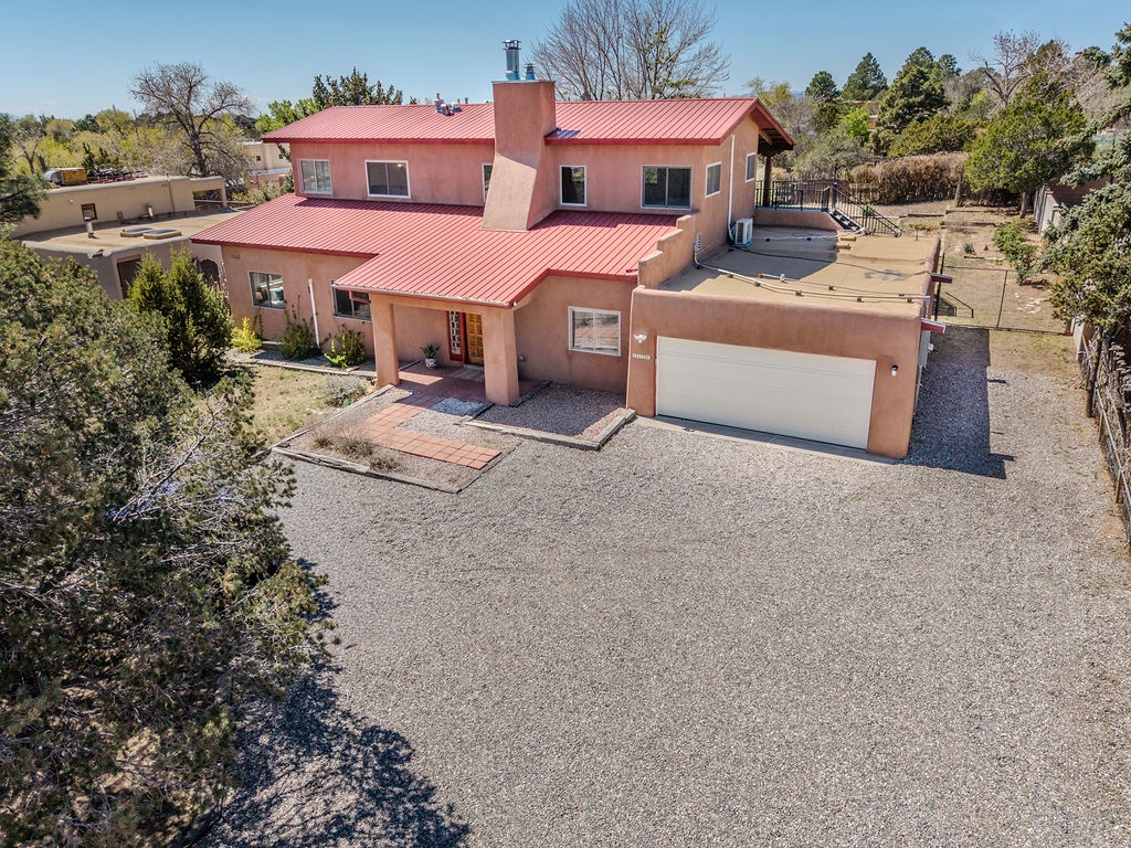 A distinctive adobe-style property with red metal roofing sits peacefully among mature trees and open space in this residential neighborhood.