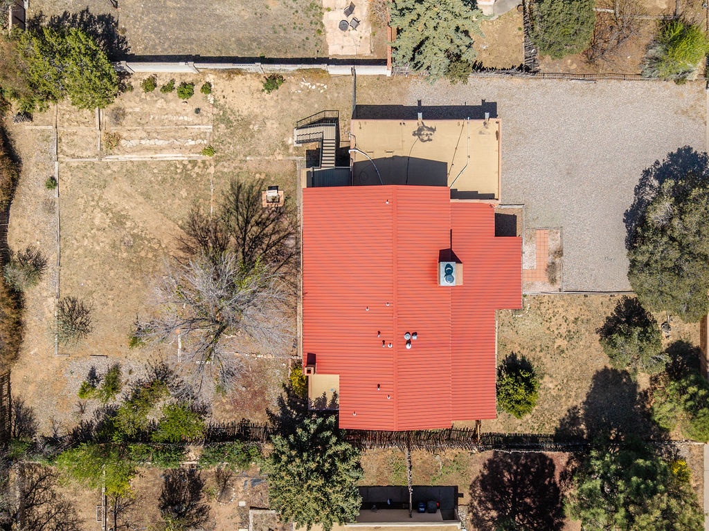 Aerial view of property featuring distinctive red metal roof surrounded by mature trees and spacious grounds.