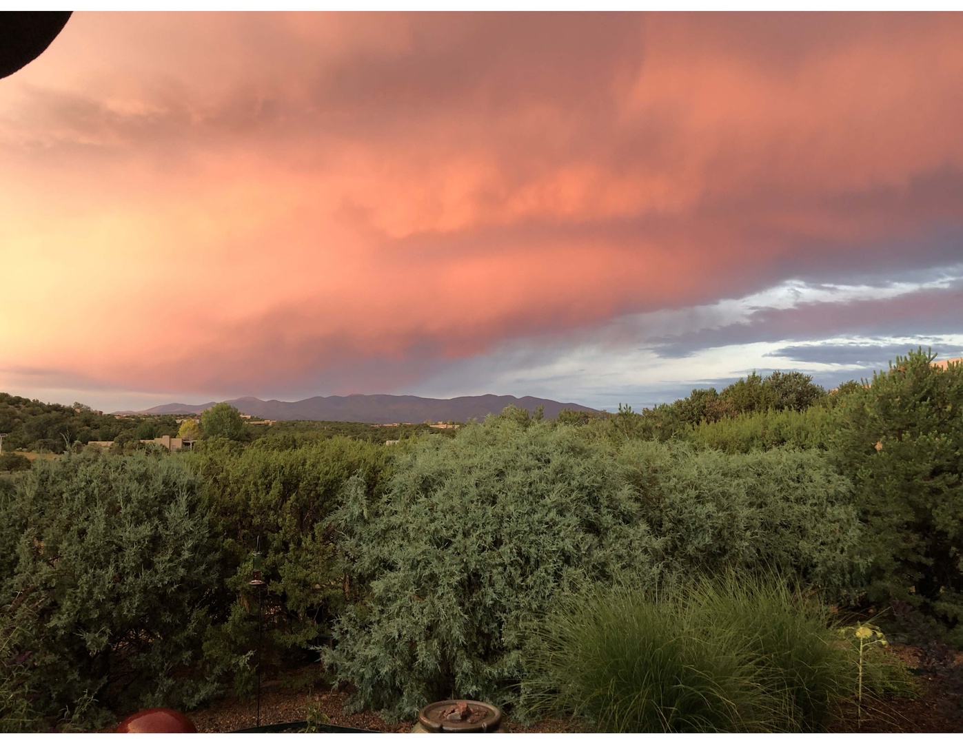 Stunning sunset paints the sky in shades of pink and coral over lush gardens and distant mountain ranges. A peaceful natural landscape surrounds the property.
