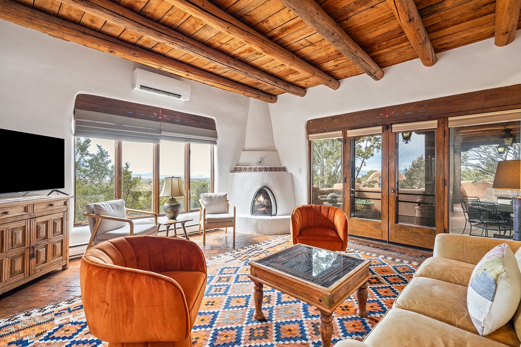 Relax in your bright living room featuring exposed wood beams, a cozy fireplace, and comfortable seating that flows seamlessly to your private patio.