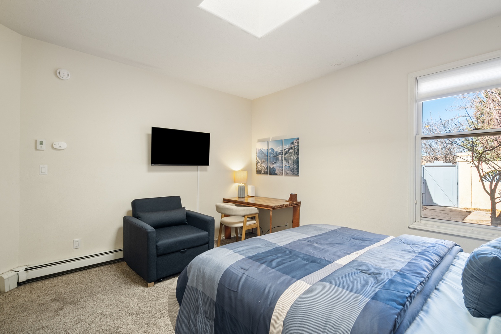 Your comfortable bedroom features a cozy reading chair, work desk, wall-mounted TV, and plenty of natural light from the skylight above for a bright, relaxing stay.