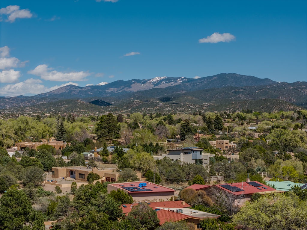 Scenic mountain landscape with residential area nestled among rolling hills and snow-capped peaks under bright blue skies.