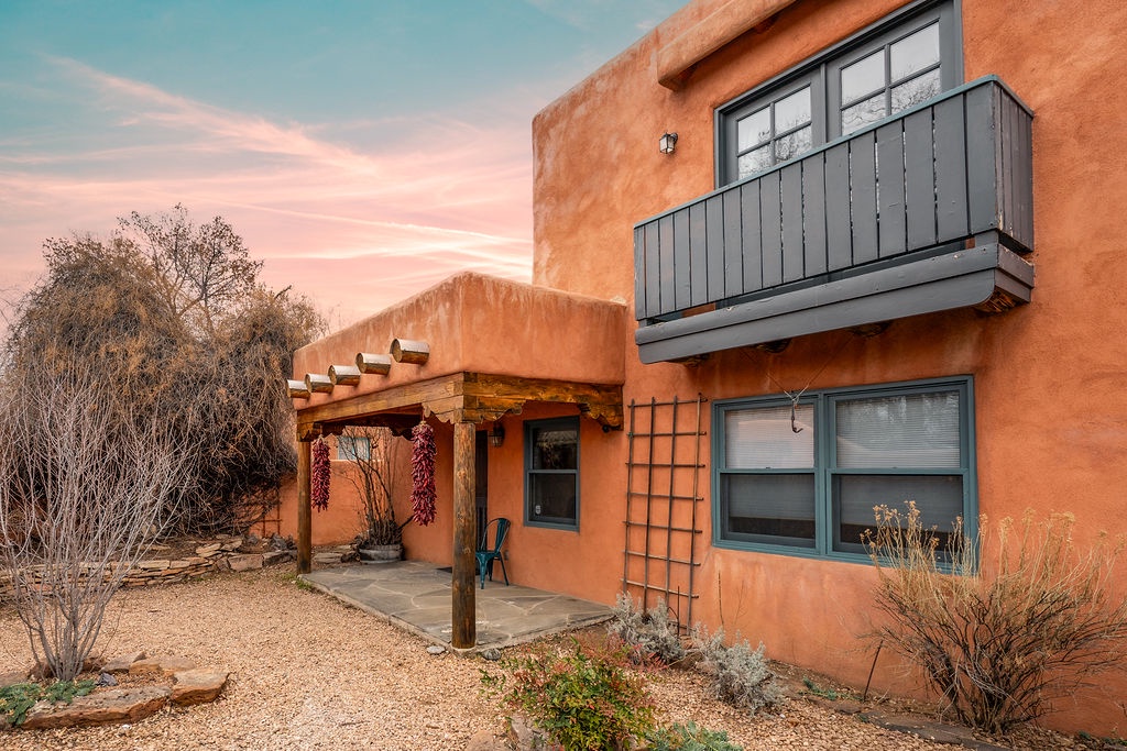 Adobe-style vacation rental with covered patio entrance and upper balcony, surrounded by native desert landscaping.