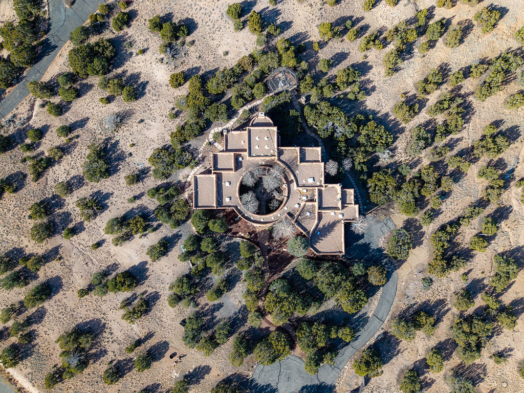 Aerial view of a distinctive circular architectural complex surrounded by natural desert landscape and scattered vegetation.