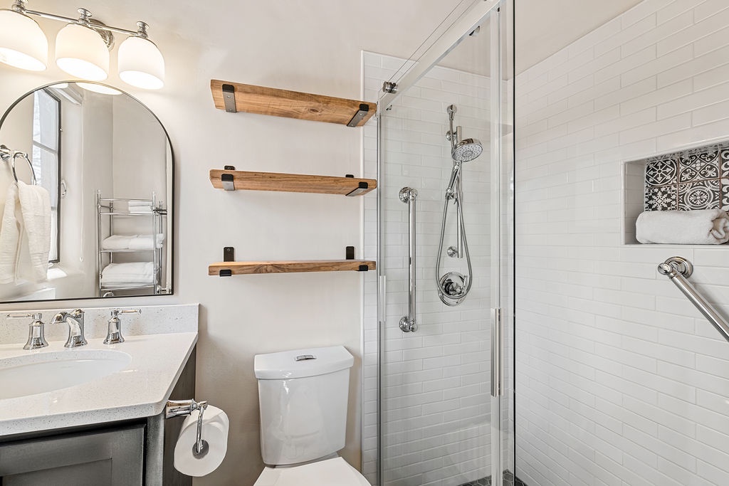 Step into your beautifully renovated bathroom featuring a spacious walk-in shower with modern fixtures and stylish floating shelves for all your essentials.