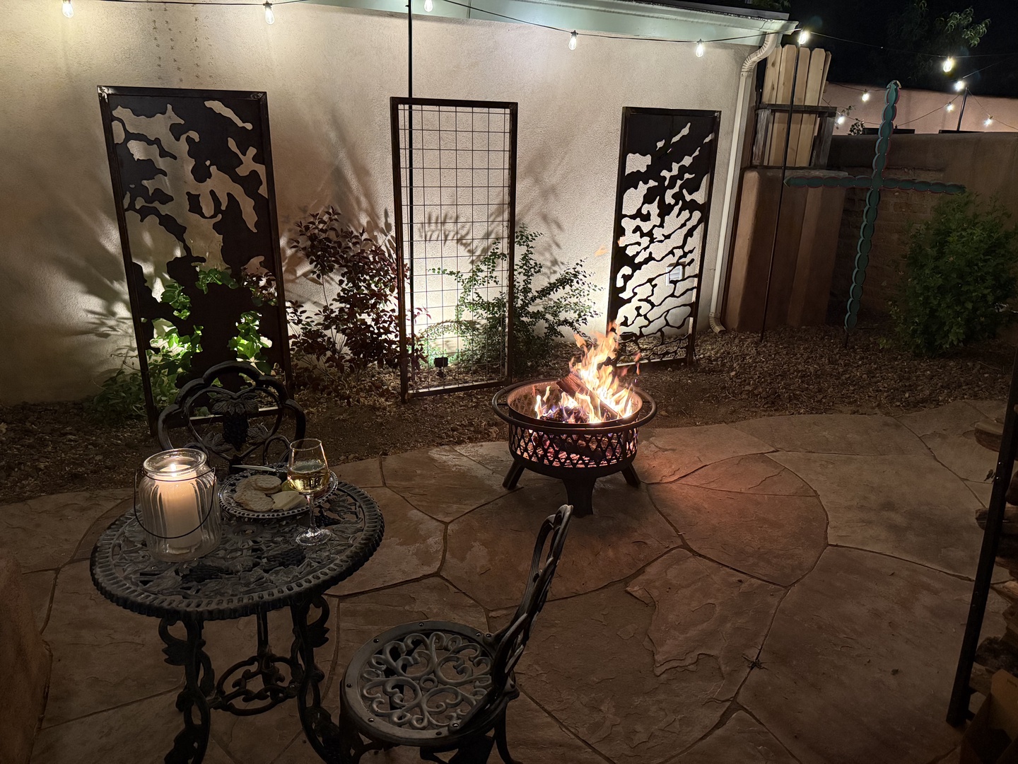 Gather around the glowing fire pit on your private patio, where string lights and artistic metal panels create a serene evening retreat perfect for unwinding under the stars.